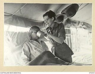 LAE, NEW GUINEA. 1944. VFX60869 SISTER W. QUIN, AUSTRALIAN ARMY NURSING SERVICE (1), GIVING A DRINK TO 95109 R/M DUJ MAN, 2/9TH GURKHA REGIMENT (2) AN EX PRISONER OF WAR OF THE JAPANESE WHO ESCAPED ..