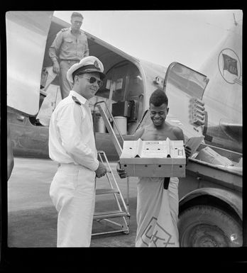 Qantas Empire Airways, Bird of Paradise service, two unidentified staff members handing over a box of [live?] chickens to a young local man, Port Moresby, Papua New Guinea