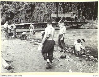 1943-09-20. NEW GUINEA. BUSO RIVER. - LAE AREA. ARMY VEHICLES CROSS A BRIDGE BUILT ACROSS THE BUSO RIVER. IN THE FOREGROUND AUSTRALIANS SOLDIERS WASH IN THE RIVER. (NEGATIVE BY H. DICK)