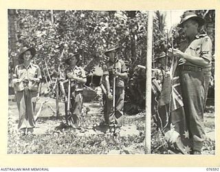 HOSKINS, NEW BRITAIN. 1944-10-13. NX11723 MAJOR G.H. LAW, 36TH INFANTRY BATTALION (5) PREPARES TO HOIST THE AUSTRALIAN FLAG WHILE THE GUARD STAND WITH THEIR RIFLES AT THE "PRESENT". IDENTIFIED ..