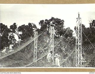 LANGWARRIN, AUSTRALIA. 1943-04. MAJOR H.C. SNELL, DIRECTOR OF SALVAGE, LAND HEADQUARTERS (RIGHT) AND MR. R. JONES, CONSTRUCTIONAL ENGINEER, INSPECTING THE SPRINGING DEVICE ON PORTION OF THE WIRE ..