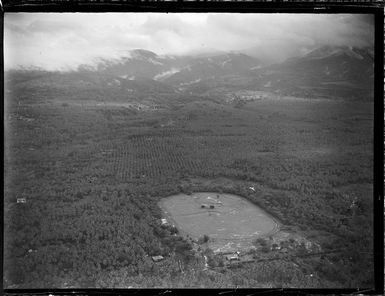 Aerial view of a [sports field?] within palm tree plantations, with forested mountains beyond, Apia, Western Samoa