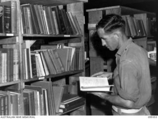 TOROKINA, BOUGAINVILLE, 1945-12-03. PRIVATE J. R. WICKHAM SELECTING A REFERENCE BOOK FROM THE LIBRARY AT THE TOROKINA REHABILITATION TRAINING CENTRE