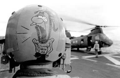 A view of the back of a flight deck crewman's helmet showing a cartoon drawing, as a CH-46 Sea Knight helicopter takes off from the amphibious assault ship USS GUAM (LPH 9), during operations off the coast of Beirut, Lebanon