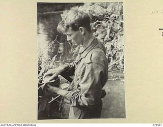 BOUGAINVILLE ISLAND, 1945-01-21. Q39645 CORPORAL K.R. ROLSTON, "D" COMPANY, 42ND INFANTRY BATTALION PLACING HIS TOBACCO AND MATCHES IN HIS BERET BEFORE MOVING OUT FROM CAMP ON A PATROL THROUGH THE ..