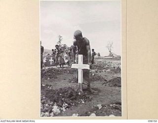 CAPE MOEM, NEW GUINEA. 1945-10-23. AN AUSTRALIAN NEW GUINEA ADMINISTRATIVE UNIT NATIVE, WORKING FOR 7 WAR GRAVES UNIT, PLACING A CROSS AT A NEW GRAVE