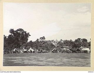 KIARIVU, NEW GUINEA, 1945-08-15. KIAP HOUSE, A NEWLY BUILT GOVERNMENT STATION PLAINLY SEEN ON THE HIGHER FEATURE ABOVE MORTAR TENTS OF 2/7 INFANTRY BATTALION WHICH ARE ESTABLISHED ON THE AIRSTRIP