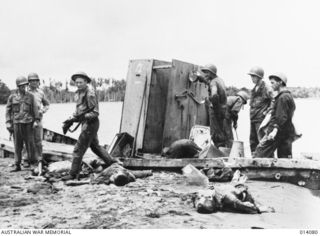 1943-01-14. PAPUA. SMASHED JAPANESE LANDING BARGE AND DEAD JAPANESE LITTER THE BEACH AT BUNA. (NEGATIVE BY BOTTOMLEY)