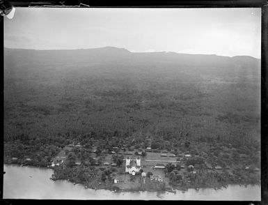 Aerial view of a coastal village with a twin tower white church and native huts, with forested mountains beyond, Apia, Western Samoa