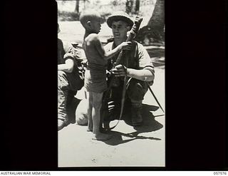 Kaiapit, New Guinea. 1943-09-25. QX38647 Private H. J. Heagney of the 2/14th Australian Infantry Battalion, AIF, shows his rifle to a small native boy