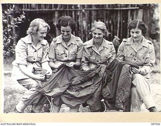 BRISBANE, QLD. 1945-02-21. MEMBERS OF THE AUSTRALIAN ARMY MEDICAL WOMEN'S SERVICE AT FRAZER'S PADDOCK EXAMINE A MOSQUITE NET FOR HOLES BEFORE THEIR EMBARKATION TO THE 2/1 GENERAL HOSPITAL AT ..