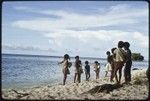 Children, several carrying infants, play on beach