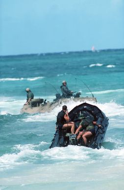 Sea-Air-Land (SEAL) team members in a rubber assault craft follow an AAVP7A1 assault amphibian vehicle heading out from the beach to return to the ships during the amphibious assault phase of Exercise RIMPAC 88