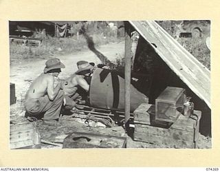 HANSA BAY, NEW GUINEA. 1944-06-22. NX102880 PRIVATE E. HEYDON (1) AND NX105409 PRIVATE R. HARRIS (2), 5TH DIVISION SALVAGE GROUP, USING A 44 GALLON DRUM TO BUILD A COOKHOUSE OVEN FOR THEIR UNIT
