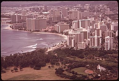 MASSED HIGHRISES OF WAIKIKI DISTRICT, FAVORITE OF TOURISTS SEEN FROM TOP OF DIAMOND HEAD, THE FAMOUS EXTINCT VOLCANO. THE WAIKIKI IMPROVEMENT ASSOCIATION HAS FORMED AN ARCHITECTURAL DESIGN REVIEW BOARD TO OVERSEE SUCH BUILDING, BUT IT IS PROBABLY TOO LATE. IN 1963 THERE WERE 9,203 HOTEL ROOMS IN ALL OF OAHU ISLAND. TODAY THERE ARE SOME 26,000 ROOMS, MOST OF THEM HERE IN WAIKIKI