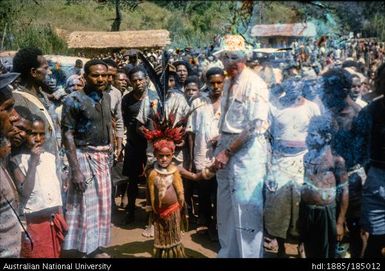 European official shaking hands with Papua New Guinean child in traditional clothing, crowd behind