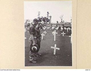 CAPE MOEM, NEW GUINEA. 1945-10-23. PRIVATE D.R.S. COMBES (1), AND PRIVATE A.M. DREVER (2), PAYING THEIR RESPECTS TO PRIVATE F.W. SHORT, ONE OF THEIR FALLEN COMRADES AT THE WEWAK WAR CEMETERY. THE ..