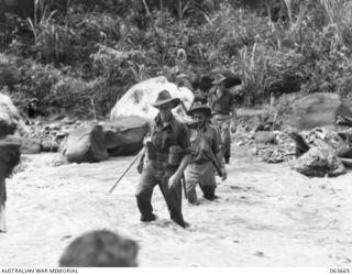 FARIA RIVER, NEW GUINEA. 1944-01-11. PERSONNEL OF B COMPANY, ACTING AS ARMED ESCORTS FOR THE NATIVE CARRIERS TAKING SUPPLIES TO THE PLATEAU FOR THE 2/9TH INFANTRY BATTALION, WADING ACROSS THE FARIA ..