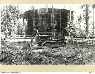 MILNE BAY, PAPUA, NEW GUINEA. 1944-04-03. A BULLDOZER PUSHING SOIL TO FORM A 'BUND', A PROTECTIVE WALL IN A CASE OF LEAKAGE, AROUND A 500,000 GALLON OIL TANK AT THE 2ND BULK PETROLEUM STORAGE ..