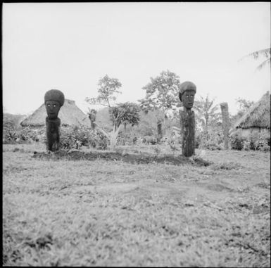 Two wooden sculptures in front of grass huts, Fiji, 1966 / Michael Terry