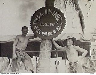 WUNUNG PLANTATION, NEW BRITAIN. 1944-12-30. QX54261 SAPPER J. T. HESS (LEFT) AND QX53744 SAPPER J. S. G. LAWRENCE 55TH FIELD PARK COMPANY, BESIDE THE UNIT SIGN PAINTED ON A LARGE CIRCULAR SAW