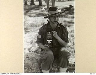 HERBERTON, QUEENSLAND, AUSTRALIA. 1944-10-11. NX40550 SERGEANT N.S MACINTYRE, 2/ 4TH INFANTRY BATTALION, HOLDS HIS AWARD, THE ORDER OF PATRIOTIC WAR FIRST CLASS. WITHIN THE CASE IS THE BOOK ..