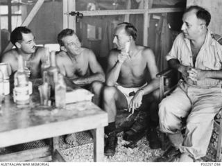 Madang, New Guinea, 1945-08-15. Sitting around a table (left) on which glasses and bottles of alcohol are resting, four RAAF officers serving with Headquarters, RAAF Northern Command (NORCOM), ..