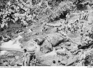 OWEN STANLEY RANGES, NEW GUINEA. C. 1942-09-01. WOUNDED AUSTRALIANS BEING CARRIED ON STRETCHERS OUT OF FORWARD BATTLE AREAS THROUGH A MOUNTAIN STREAM BY NATIVE BEARERS (FUZZY WUZZY ANGELS)