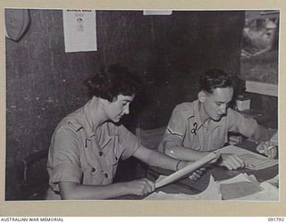 LAE, NEW GUINEA. 1945-05-15. GUNNER G. FLETCHER (1), WORKING FOR THE ASSISTANT MILITARY SECRETARY, HEADQUARTERS FIRST ARMY, IS ASSISTED BY CORPORAL K.A. REYNOLDS (2), ON DRAFT MEMOS FOR LAND ..