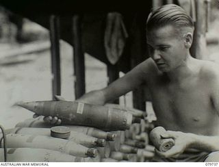 Pearl Ridge, Bougainville. 1945-03-08. NX103226 Sergeant (Sgt) L. Bell of the 4th Australian Field Regiment unloading a smoke charge prior to placing propaganda leaflets in cardboard container to ..