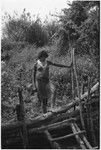 Woman in barkcloth cap and shell valuable necklace climbs over a fence