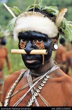 Portrait of a Febi youth with a distinctive face paint pattern of red and yellow ochre over the usual black/ charcoal background colour