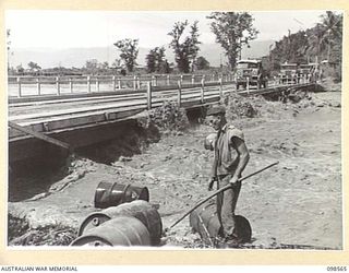 LAE, NEW GUINEA. 1945-10-14. A MEMBER OF THE FIRST ARMY SALVAGING 44-GALLON DRUMS WHICH WERE CARRIED DOWN THE BUTIBUM RIVER WHEN IT OVERFLOWED ITS BANKS DURING HEAVY RAIN. IT FLOODED THE ROAD AND ..