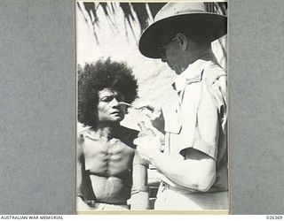 NEW GUINEA. 1942-08. A MEDICAL ORDERLY WARRANT OFFICER II. J.N. WALSHE, OF THE NATIVE MEDICAL SERVICES PAINTING THE CHEEKS OF A FUZZY-HAIRED NATIVE WHO HAS BEEN AFFECTED BY FACIAL TINEA