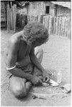 Iika chipping edges off of coneshells with a knife, one step in making kofu shell money beads, at Fanuaba'ita