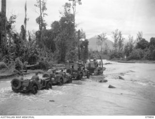 BOUGAINVILLE, SOLOMON ISLANDS. 1945-03-19. JEEPS OF THE 58/59TH INFANTRY BATTALION BEING TOWED BY A TRACTOR THROUGH A FLOODED AREA OF THE TOROKINA RIVER