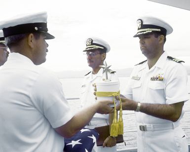MCPO Charles Cartwright presents the urn containing the remains of CDR Harold Schwartz to CDR Robert James, commanding officer of the tank landing ship USS RACINE, during burial at sea services for the retired Navy doctor. Schwartz served as a doctor assigned to the Paratroop Battalion, 1ST Marine Division and took part in combat operations on Guadalcanal, the Gilbert Islands, Marshall Islands and Okinawa. The RACINE is anchored at Iron Bottom Sound off Guadalcanal during the ceremony