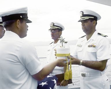 MCPO Charles Cartwright presents the urn containing the remains of CDR Harold Schwartz to CDR Robert James, commanding officer of the tank landing ship USS RACINE, during burial at sea services for the retired Navy doctor. Schwartz served as a doctor assigned to the Paratroop Battalion, 1ST Marine Division and took part in combat operations on Guadalcanal, the Gilbert Islands, Marshall Islands and Okinawa. The RACINE is anchored at Iron Bottom Sound off Guadalcanal during the ceremony