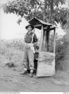 RABAUL, NEW BRITAIN. 1945-09-14. CORPORAL D. HAMILL, 11 DIVISION PROVOST COMPANY, STANDING OUTSIDE A JAPANESE SENTRY BOX AT AN INTERSECTION IN RABAUL TOWNSHIP. TROOPS OF 4 INFANTRY BRIGADE ARE ..