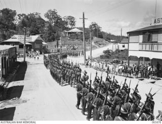 HERBERTON, QLD. 1944-04-25. PERSONNEL OF THE 6TH DIVISION, LED BY THE BAND OF THE 2/2ND INFANTRY BATTALION, MARCHING ALONG THE MAIN STREET TO THE WAR MEMORIAL FOR THE ANZAC DAY SERVICE