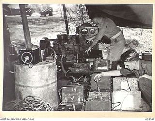 CAPE WOM, WEWAK AREA, NEW GUINEA, 1945-08-14. MEMBERS OF 6 DIVISION SIGNALS MONITORING THE CHARGING OF BATTERIES. CORPORAL R.B. LEGGETT (1), ADJUSTS SWITCHBOARD OF CHARGING MOTOR WHILE SIGNALMAN ..
