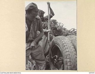 WEWAK AREA, NEW GUINEA. 1945-10-13. CRAFTSMAN L. HOTCHIN (1) AND CRAFTSMAN R.J. BUNT (2), MEMBERS OF 3 MOBILE TYRE WORKSHOP SECTION, REMOVING RIM BOLTS FROM JAPANESE TRUCK WHEELS TO OBTAIN THE ..