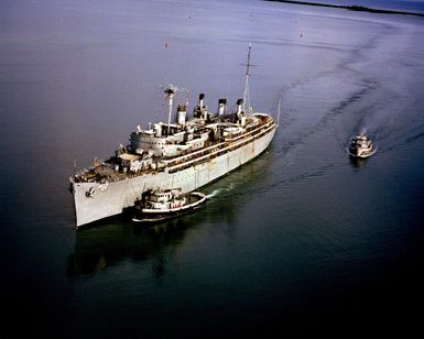 A port bow view of the repair ship USS JASON (AR 8) as the large harbor tug NOGALES (YTB 777) and another tug approach to assist the vessel into port