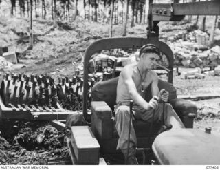 PALMALMAL PLANTATION, NEW BRITAIN. 1944-11-29. WX15792 LANCE-CORPORAL C.F. HARVEY, 2/3RD RAILWAY CONSTRUCTION COMPANY, 48TH DEPUTY COMMANDER ROYAL ENGINEERS (WORKS) USING A HEAVY TRACTOR TO HAUL A ..