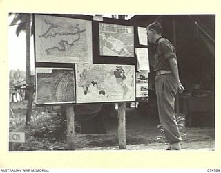 MILILAT, NEW GUINEA. 1944. A SOLDIER STUDYING THE NOTICE BOARD OF THE ARMY EDUCATION SERVICE AT HEADQUARTERS, 5TH DIVISION