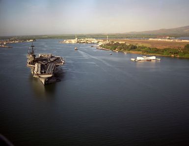 An aerial bow view of the US Navy (USN) Forrestal Class Aircraft Carrier USS RANGER (CV 61), with her Sailors manning the rails and aircraft of the Carrier Air Wing 2 (CVW-2) on her deck, being nudged by tugboat NIANTIC (YTB-781) and another tugboat, as she arrives at Pearl Harbor Naval Base in Pearl Harbor, Hawaii (HI). In the background is the USS ARIZONA (BB 39) Memorial and Ford Island