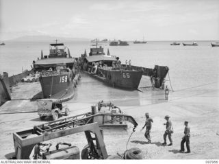 WEWAK BEACH, NEW GUINEA. 1945-10-18. LANDING CRAFT, TANK (LCT) LINED UP ON THE BEACHHEAD WITH VARIOUS SUPPLY CRAFT IN HARBOUR IN BACKGROUND. THE LIBERTY SHIP SAM FOYLE (IN BACKGROUND) BROUGHT 9,000 ..