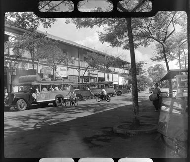 Street scene in Papeete, Tahiti, showing a bus full of passengers and empty buses parked along side the road