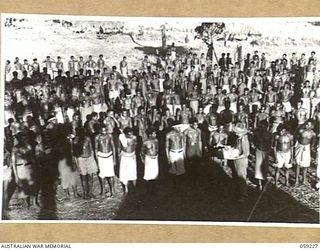 KUMBARUM, NEW GUINEA, 1943-10-23. GROUP OF NATIVE BOYS RECEIVING THEIR RATION OF TOBACCO AND MATCHES AT THEIR EVENING LINE UP AT HEADQUARTERS, 7TH AUSTRALIAN DIVISION AREA