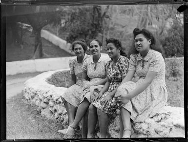 Four unidentified local girls sit on a stone wall, Rarotonga, Cook Islands